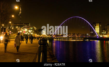 Newcastle Upon Tyne, England, Regno Unito, 17 novembre 2018. Vista dalla banchina del porto con la gente a piedi lungo il Fiume Tyne del pedone Gateshead Millennium Bridge e la Rank Hovis ha Baltic mulino di farina ora Baltic Centre for Contemporary Art pit fino a notte con riflessi nell'acqua Foto Stock