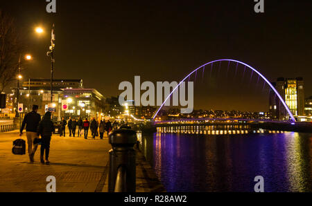 Newcastle Upon Tyne, England, Regno Unito, 17 novembre 2018. Vista dalla banchina del porto con la gente a piedi lungo il Fiume Tyne del pedone Gateshead Millennium Bridge e la Rank Hovis ha Baltic mulino di farina ora Baltic Centre for Contemporary Art pit fino a notte con riflessi nell'acqua Foto Stock