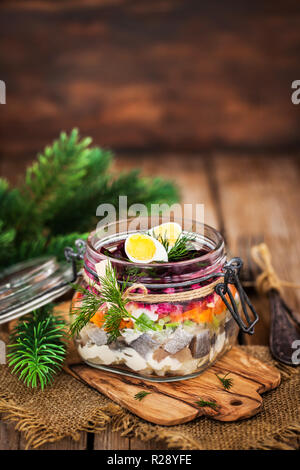 Tradizionale russo betroot stratificata e insalata di aringa (sotto una pelliccia) in un barattolo di vetro, legno rustico sfondo, il fuoco selettivo Foto Stock