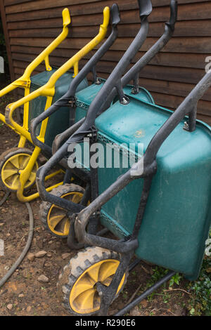 Tre temperato carriole di plastica allineati ed in appoggio o appoggiarsi contro la tettoia in legno parete nella zona del giardino all'aperto Foto Stock