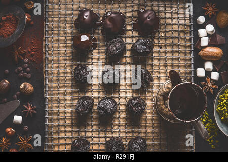 Praline fatte in casa e il tartufo in cucina scuro sfondo tabella con cioccolato fondente e ingredienti, vista dall'alto Foto Stock