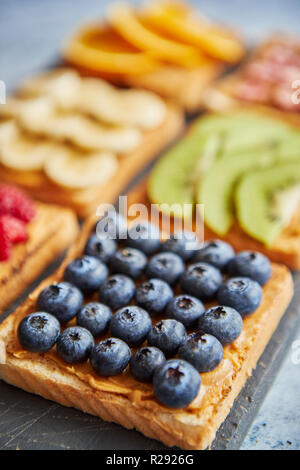 Sei fette biscottate con burro di arachidi, frutta fresca su un livello di grigio ardesia Foto Stock