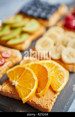 Sei fette biscottate con burro di arachidi, frutta fresca su un livello di grigio ardesia Foto Stock