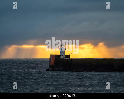 Sunrise dietro un piccolo faro presso il molo del porto di Aberdeen. Foto Stock