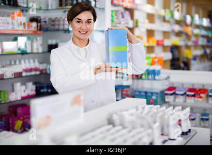 Felice farmacista femmina suggerendo utili prodotti per la cura del corpo in farmacia Foto Stock