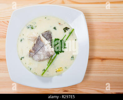 Vista superiore della zuppa scozzese affumicato con eglefino, patate e cipolle (cullen skink) servita nella piastra bianca con verdi su sfondo di legno Foto Stock