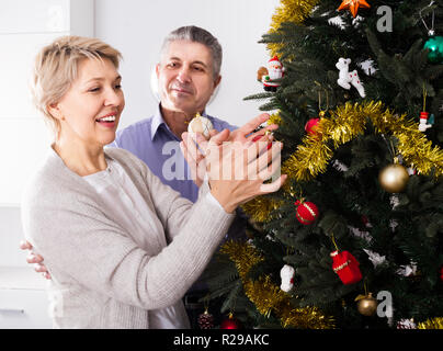 Donna e uomo 50-55 anni sono riagganciare Nuovo Anno di giocattoli su un abete bianco prima di Natale. Foto Stock