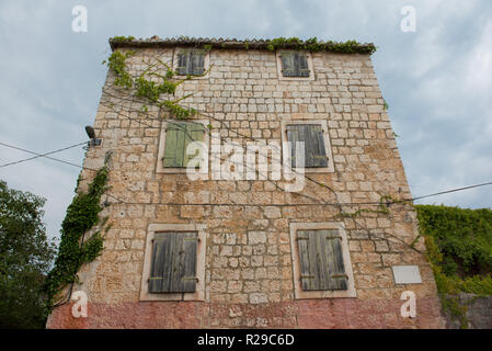 E la vecchia casa abbandonata in pietra con chiusura finestre in legno. Cielo blu con nuvole in background. Vintage casa sul mare. Foto Stock