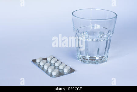 Bicchiere di acqua e pillole di bianco in blister. Vitamine. Antibiotici. Foto Stock