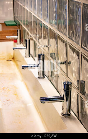 Un bacino di sporco nel bagno pubblico. Lungo lavandino con una fila di rubinetti di acqua. Foto Stock