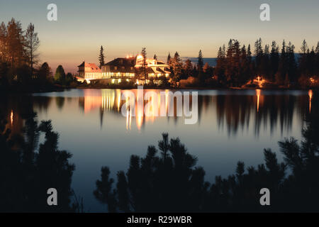 Pittoresca vista autunnale del lago il villaggio di Strbske Pleso negli Alti Tatra National Park, Slovacchia. L'acqua chiara con riflessi di alberghi illuminata sullo sfondo Foto Stock