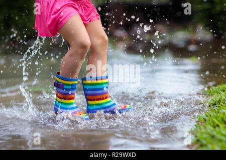 Kid giocando fuori sotto la pioggia. I bambini con ombrellone e stivali da pioggia giocare all'aperto sotto la pioggia. Ragazzina salta nella pozza di fango. Kids Fun da rainy Foto Stock