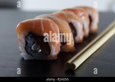 Delizioso sushi fresco panini con salmone e crema di formaggio sulla piastra nera. Tradizionale cibo giapponese, cibo sano concetto. Foto Stock