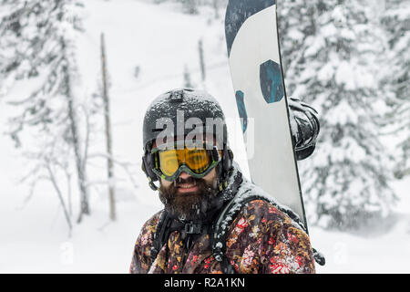 Ritratto di uomo barbuto occhiali da sci snowboard di contenimento in montagna Foto Stock