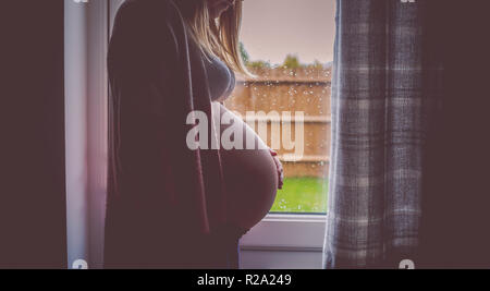 Vista laterale della donna incinta si fermò davanti alla finestra Foto Stock