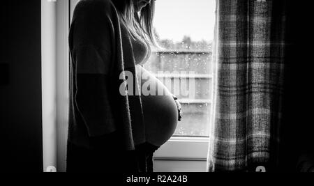 Vista laterale della donna incinta si fermò davanti alla finestra Foto Stock