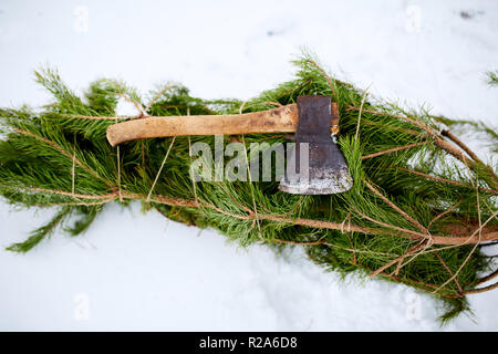 Ax sul tagliare abete rosso o pino albero di natale succursali sul terreno innevato. La deforestazione divieto. Un comportamento irresponsabile verso la natura, mantenere verde, salvare il concetto di foresta. Foto Stock