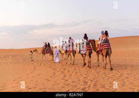 Camel caravan con i turisti sulle dune di sabbia avventura nel deserto di Dubai. Foto Stock