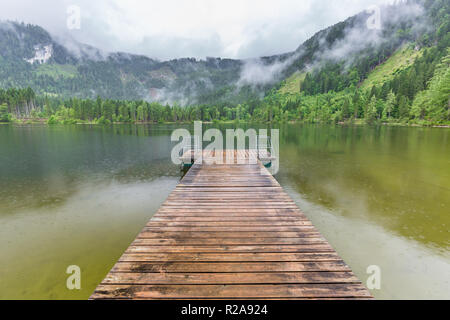 Lago di montagna paesaggio, uno splendido scenario con le nuvole e alberi di pino oltre il lago di riflessione Foto Stock