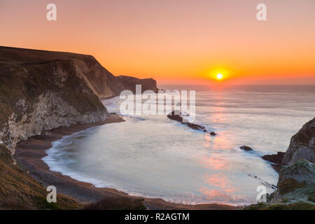 Lulworth, Dorset, Regno Unito. Il 18 novembre 2018. Il sole sorge sull uomo O'guerra bay su Jurassic Coast di Dorset nei pressi di Lulworth su una chiara fredda mattina. Credito Foto: Graham Hunt/Alamy Live News. Foto Stock
