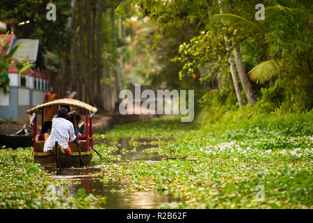 Alcuni turisti sono su una barca a vela canoa sui lussureggianti e verdi backwaters di Alleppey durante il tramonto, Kerala, India. Foto Stock