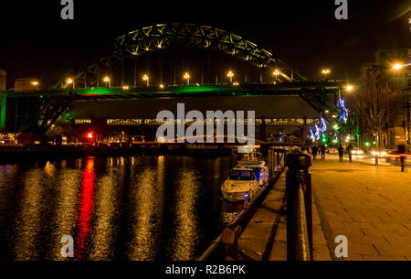 Fiume Tyne durante la notte con le luci sul ponte girevole, livello elevato di Bridge e Tyne Bridge e la gente che camminava sul lungofiume, Newcastle, England, Regno Unito Foto Stock