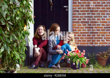 Felice la madre e le figlie sedersi sotto il portico della loro casa Foto Stock