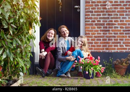 Felice la madre e le figlie sedersi sotto il portico della loro casa Foto Stock