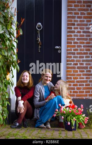 Felice la madre e le figlie sedersi sotto il portico della loro casa Foto Stock