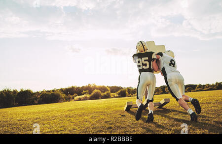 Due giovane giocatore di football americano affronta la pratica e trapani difensivo esterno su un campo sportivo nel pomeriggio Foto Stock