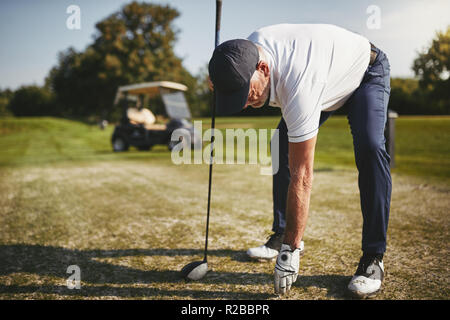 Sportivo da uomo senior ponendo una sfera su un raccordo a T durante la riproduzione di un round di golf in una giornata di sole Foto Stock