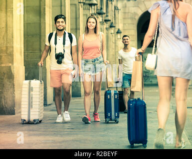 Le persone felici turisti tenendo a piedi e trascinando i bagagli in città per le vacanze Foto Stock