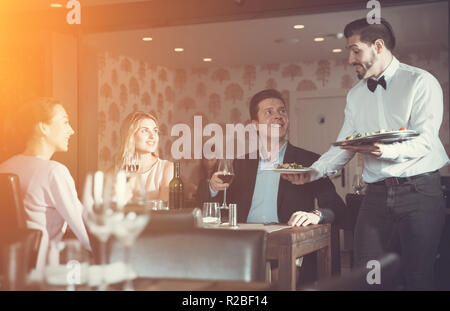 Giovane cameriere che serve pasti al cordiale compagnia presso il ristorante Foto Stock