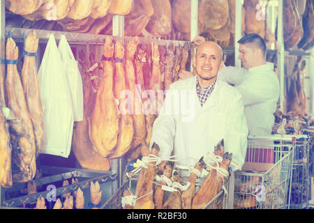 Due ispettori sorridente in tute bianche controllo qualità di jamon giunti presso la fabbrica Foto Stock