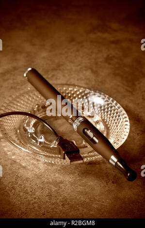 Tonalità seppia Sigaretta elettronica con adattatore C/A e posacenere su un tavolo Foto Stock
