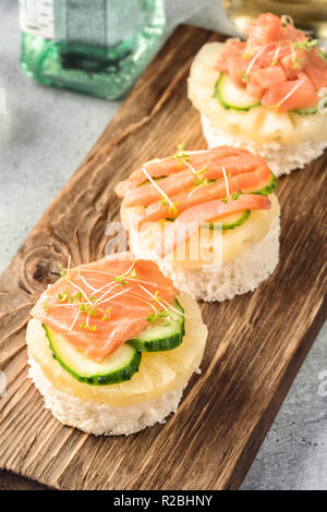 La bruschetta toast di pane bianco con le fette di ananas cetriolo pescare il salmone fresco e i cavoli verdi. Servita su legno che serve nella tabella della scheda con Apple Foto Stock