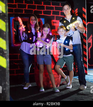 Ritratto di felici i bambini ed i loro genitori con le pistole laser durante il gioco lasertag in dark room Foto Stock