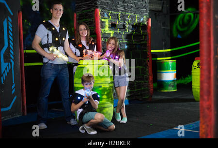 Ritratto di felici i bambini ed i loro genitori con le pistole laser durante il gioco lasertag in dark room Foto Stock