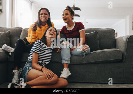 Tre giovani ragazze seduti insieme a casa a guardare la televisione e ridere. Le ragazze adolescenti a sleepover divertirsi guardando la TV seduto in soggiorno Foto Stock