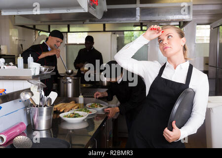 Infelice e stanco giovane cameriera in attesa ordinato piatti nel ristorante cucina Foto Stock