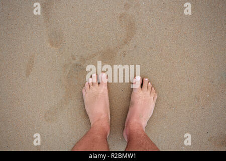 Gli uomini i piedi sulla sabbia. vista superiore dei piedini maschio su di una spiaggia di sabbia con impronte Foto Stock