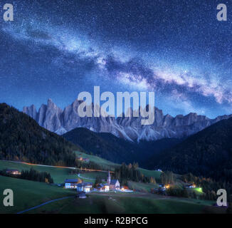 Santa Maddalena e via lattea di notte in autunno in Italia. Cielo stellato con via lattea oltre a Santa Maddalena e le montagne. Villaggio con case, chiesa, gr Foto Stock
