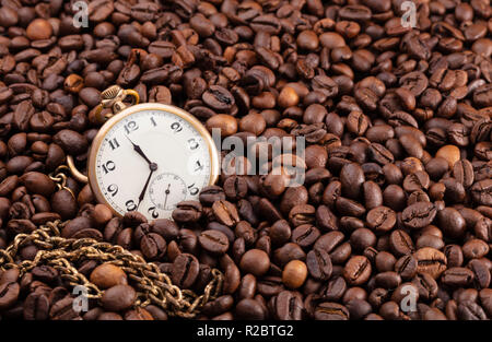 Il vecchio orologio da tasca, dorate con una lunga catena su un mucchio di chicchi di caffè, concettuale che mostra fotografica che ogni momento è buono per un caffè Foto Stock