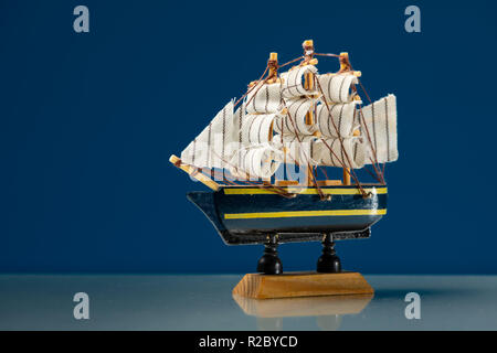 Primo piano di un piccolo modello in legno di una nave a vela, sfondo blu Foto Stock