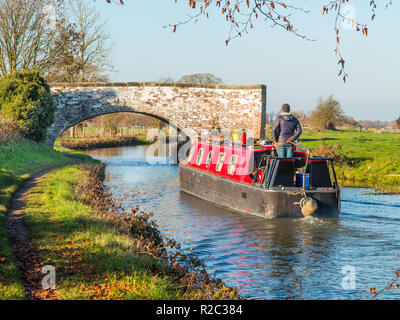 Uomo che guida un narrowboat lungo il canale di Trent e Mersey nella campagna di Hassall Green nel Cheshire, Inghilterra, Regno Unito Foto Stock