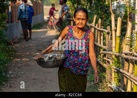 Don Det, Laos - Aprile 24, 2018: donna locale a piedi attraverso un villaggio e portante un recipiente metallico pieno di pesce fresco Foto Stock