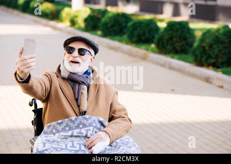 Felice senior uomo disabili in carrozzella assumendo selfie su strada Foto Stock