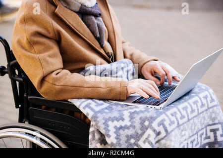 Ritagliato colpo di uomo disabili in carrozzella utilizzando portatile su strada Foto Stock