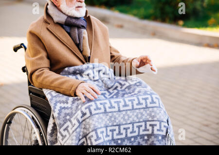 Ritagliato colpo di senior uomo disabili in carrozzella con plaid sulle gambe su strada Foto Stock