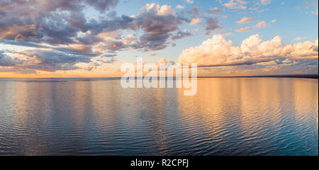 Le nuvole riflettono in mare calmo al tramonto dorato - antenna minimalista panorama Foto Stock